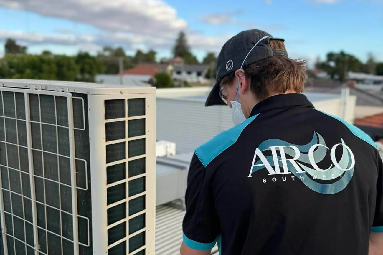AirCo South West technician inspecting an outdoor air conditioning condenser unit on a rooftop